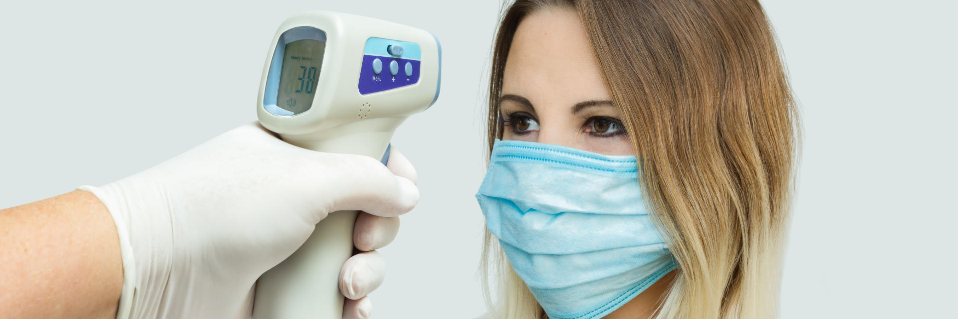 A woman wearing a medical mask having the temperature taken.